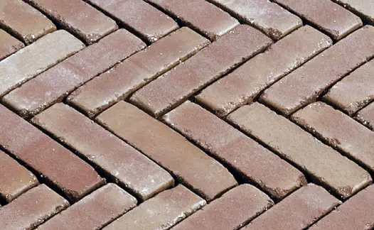 Section of Roma brick pavers laid herringbone pattern with wide, unsanded joints, showing tumbled edges and tonal variation.
