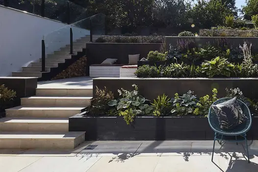 A sunken courtyard showing 3 tiers of a modern garden, with bullnosed porcelain steps, and retaining walls, with planting behind.