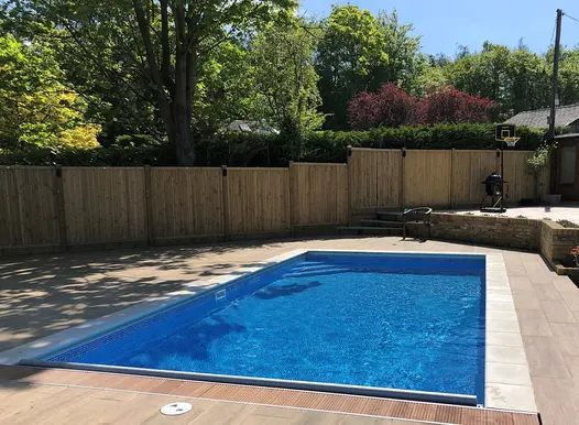 Swimming pool in a back garden with Rovere wood effect porcelain paving surround and closed board fencing panel boundary.