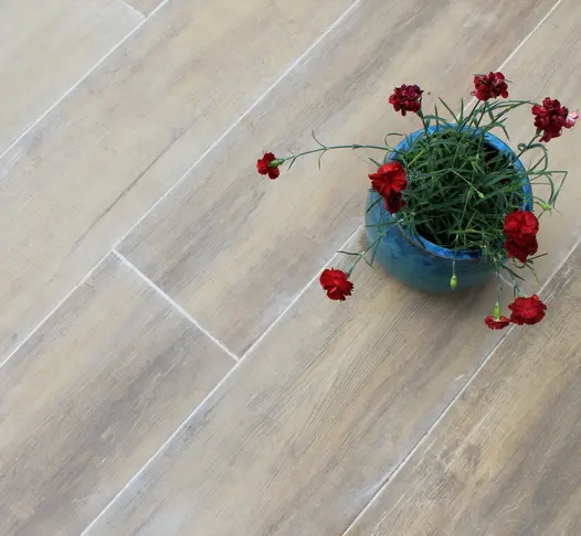 Blue plant pot planted with red flowers sitting on top of Rovere wood effect porcelain outdoor tiles grouted with a light grey grout.