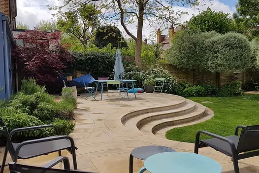 bespoke curved pieces of harvest smooth sandstone paving create unique patio and steps in densely planted garden.