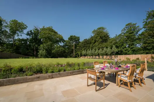 Large rectangular patio of Harvest smooth sandstone in huge garden, mostly down to grass, with sleepers at edge of paving.