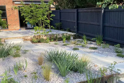 Elevated patio using dove grey sawn sandstone paving leads down with step to pebbled area with desert style planting.