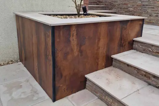 3 steps with risers of stone cladding ascend past deep planted bed faced with Siena Copper compact DesignClad external porcelain.