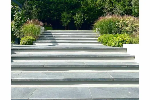 Slab Coke Porcelain Paving used as steps leading up to lawn area with bushes surrounding up the levels. Shadows dance in the background.