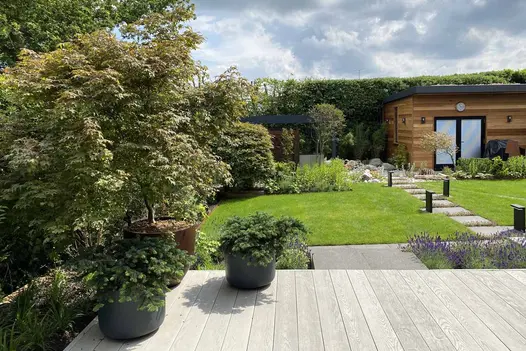Composite deck of Smoked Oak Millboard looks out over lawned garden with straight path of square stepping stones to studio.