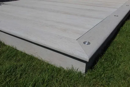 Lawn on 2 sides of corner of Smoked Oak Millboard composite deck, showing mitred edge boards and lights flush with surface.