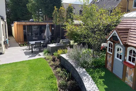 Curved wall with steel grey porcelain smooth coping and black cladding leads to dining area and from childs playhouse.