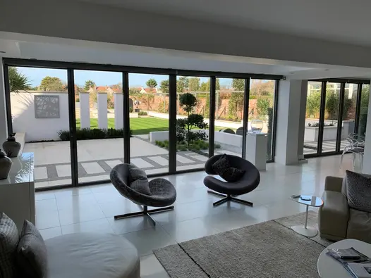 View through wide bifold doors from inside monochrome room to huge modern garden with lawn and Harvest sawn sandstone paving