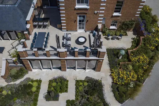 Overhead view. Harvest sawn sandstone patio sits above garden on roof of house extension. Steps down to planted area. 