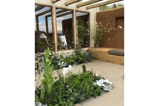 3 windows overlook Heath sawn sandstone patio with adobe-style wall and bench and thickly planted beds. Design by Jessica Makins.