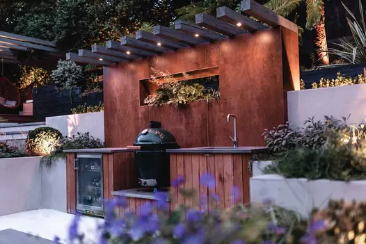 Outdoor kitchen with sink, wine cooler and barbecue, beneath large splashback faced with Steel Corten external cladding.