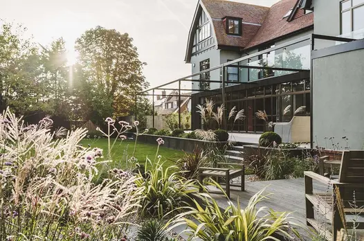 Steps descend from patio between raised beds faced with Steel Dark external cladding to lawn below with deck area.