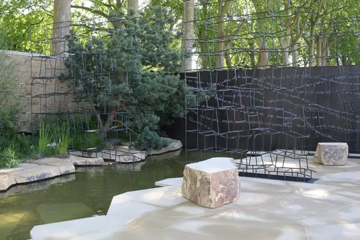 Jagged shapes edge long pond in Chelsea show garden with open metal structure in front of Steel Dark porcelain clad wall.
