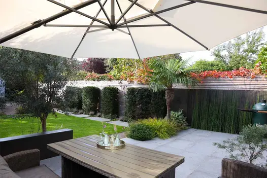 Steel Dark Luxury DesignClad faces low wall separating patio with sofa and wooden table under parasol from rectangular lawn.