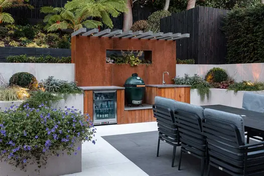 Outdoor entertaining space with an outdoor kitchen, dining table and paved with light grey and steel grey porcelain.