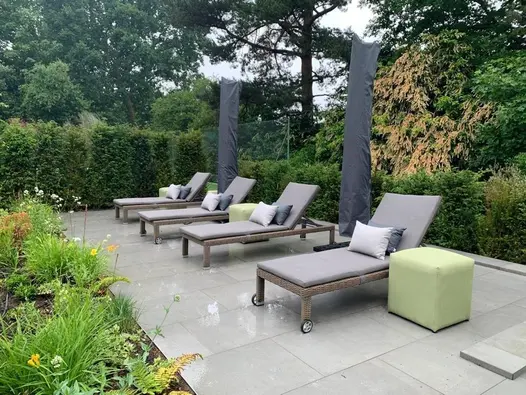 Steel Grey porcelain patio with 4 sun loungers, parasols and surrounded on all sides by established shrubs and hedging.