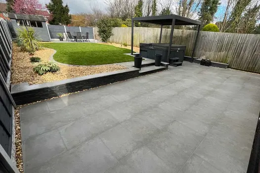 Large patio of steel grey porcelain with 2 steps leading up to lawn and dining area, smooth coping divides.