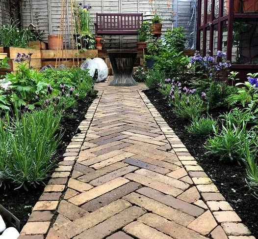 Herringbone pattern path of Aldridge and Westminster Clay Pavers between 2 lavender-edged borders towards round table.