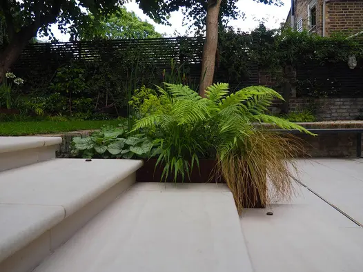 Faro Porcelain 36mm Bullnose Steps in close up view leading down from lawn featuring plant in corten steel planter.
