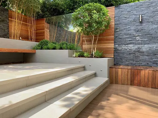 Cream steps lead down to a Traditional DesignBoard decking area, framed by stone-clad walls and raised planter beds.
