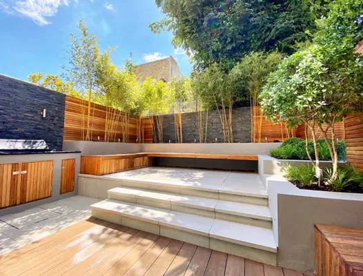 Cream steps lead away from a Traditional DesignBoard decking area, surrounded by stone-clad walls and raised planter beds.
