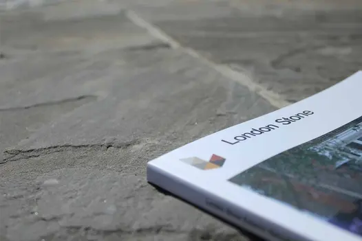 Close up of Tumbled Black Indian sandstone paving, showing riven texture, with London Stone catalogue lying on right. 