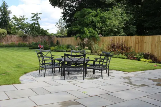 Large garden mostly put down to lawn, flower border against fence, metal garden furniture on Kandla Grey Indian sandstone paving.