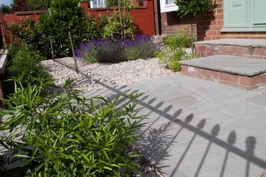 Shadow of iron railings fall on front garden paved in white gravel with Kandla Grey tumbled sandstone paving and steps to front door.