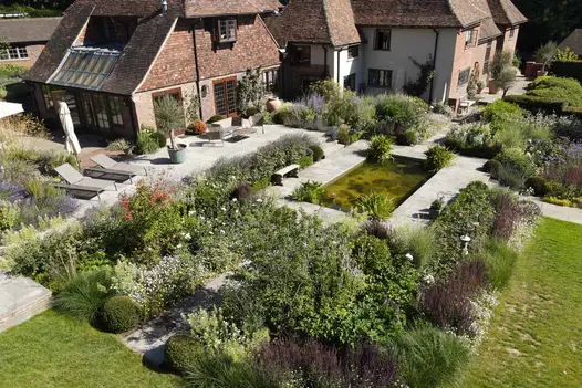 Tumbled Black Sandstone paving encircling a central pond, with sunloungers and table and chairs on the left, all surrounded by planting.