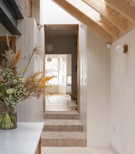 White-painted narrow interior with 3 steps of Westminster Clay Pavers up to large, light-filled, wood-floored room. 
