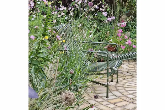 Two green metal armchairs sit on Mint Sandstone Setts, surrounded by trees, shrubs, and lush greenery.