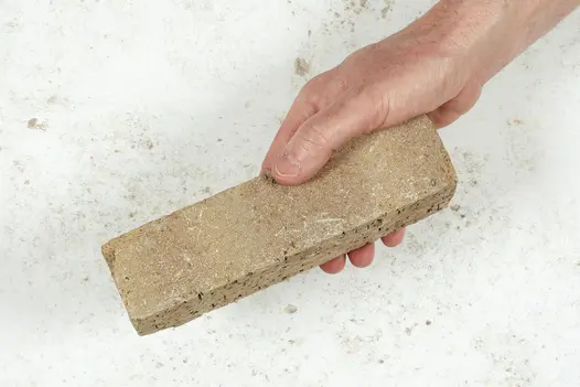Hand holding 1 buff Westminster clay paver, showing the textures of the edge and the flat faces. Free UK delivery available.